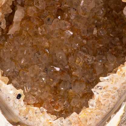Agaat geode uit Brazilië op zwarte standaard met witte kristallen en een zachte oranje gloed.