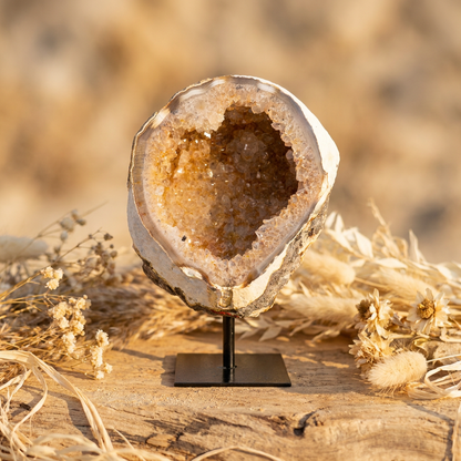 Agaat geode uit Brazilië op zwarte standaard met witte kristallen en een zachte oranje gloed.